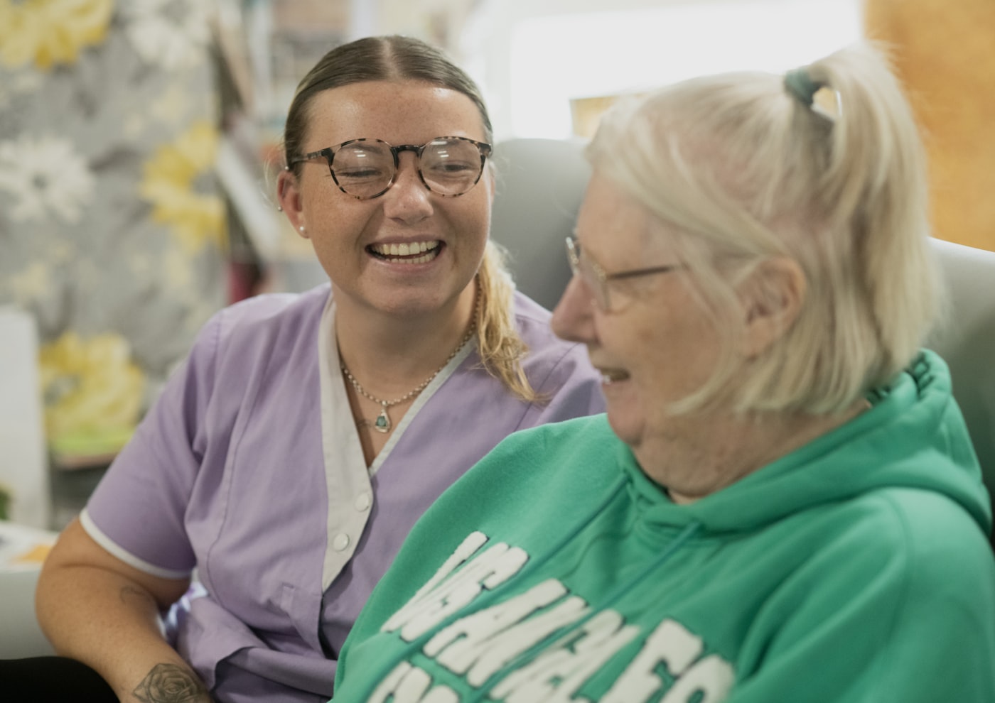 A caregiver and an elderly woman laughing together at home
